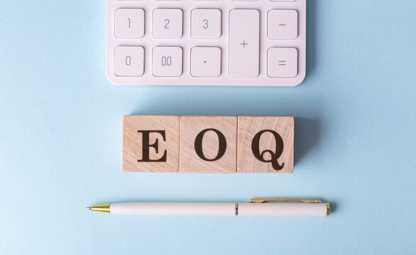 EOQ word on wooden block with pen and calculator on blue background