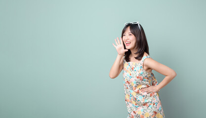 Happy Asian woman with sun glasses shouting above casual dress poses against pastel green background blank copy space for advertising content promotion