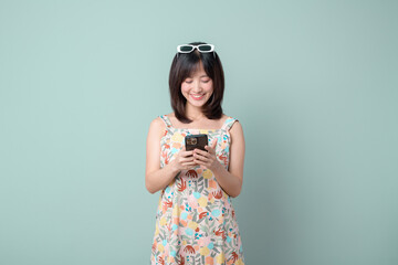 Happy Asian woman using a mobile phone isolated on pastel green background.