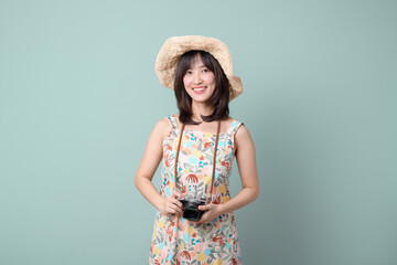 Happy Asian woman wearing casual dress and hat with camera on vacation or travel theme isolated on pastel green background. Travel and vacation concept.
