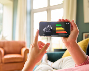 Close Up Of Woman Looking At Screen Of Energy Efficiency Meter On Mobile Phone Lying On Sofa At Home