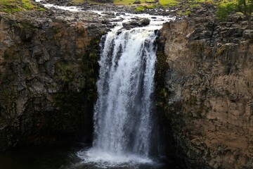 Obraz premium a waterfall flowing from a rock into a river with green trees