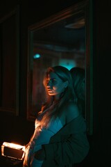 Conceptual night portrait of a woman leaning against a mirror, holding a light on her hands