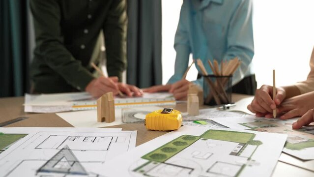 Smart architect and safety engineer discussion about building blueprint on table with architectural document, measurement tools and wooden block scatter around at modern office. Closeup. Delineation.