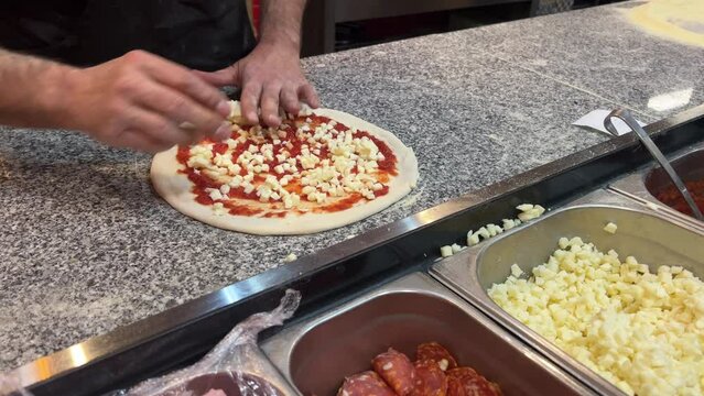 chef sprinking cheese and meat on pizza. close up putting meat