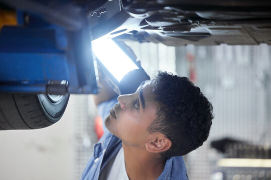 Man, mechanic and bottom of car with light in workshop for working or maintenance, inspection and oil change. Person, motor and garage for engine or exhaust diagnostics, transmission and brake repair
