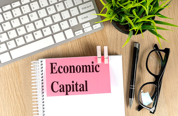 ECONOMIC CAPITAL text pink sticky on notebook with keyboard, pen and glasses