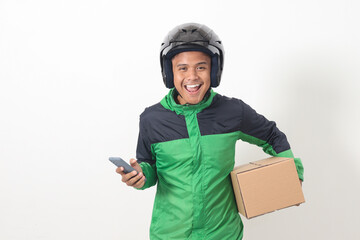 Portrait of Asian online courier driver wearing green jacket and helmet delivering package and box for customer while using mobile phone and taking order. Isolated image on white background