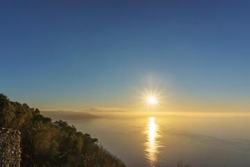 Mediterranean bay seen from Monte Sant'Elia viewpoint during sunset with smoke rising up from...