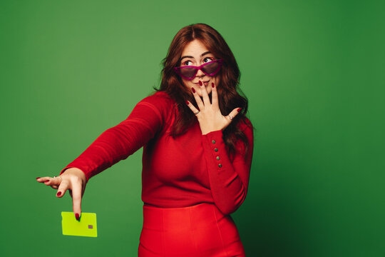 Young woman with sunglasses holding a green credit card on a vibrant green background