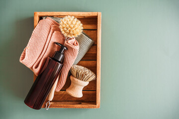 Ein Seifenspender, eine Reinigungsbürste und Putztücker in einer Holz Kiste. Draufsicht, jadegrüner Hintergrund, Zero Waste.