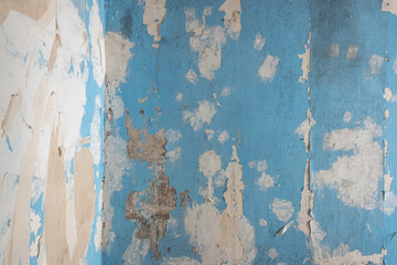 old peeling and weathered wall with several layers of paint under the blue layer