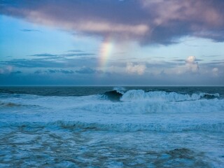 waves break into shore and beich with a rainbow in the sky