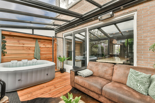 Modern glass-enclosed patio with hot tub and cozy sofa