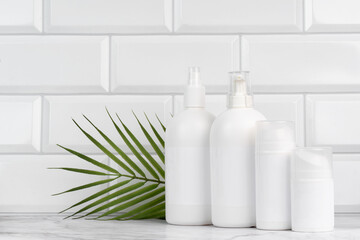 White cosmetic bottles with natural palm leaf on marble