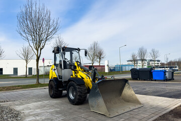 New yellow forklift standing on freshly laid road tiles. Trash cans in the background.