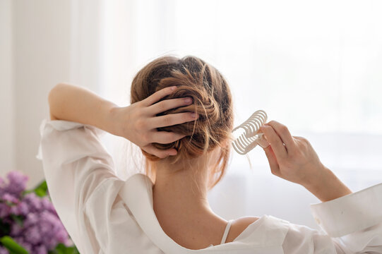 Young woman making messy hair bun, clipping hair with claw clip, back view, soft natural light, fashion hairstyle, girls daily beauty routine, lifestyle