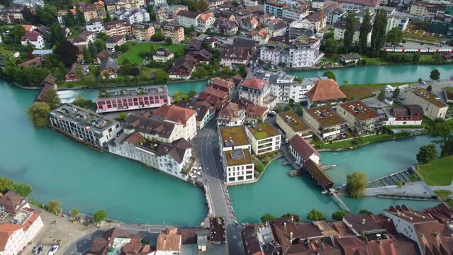 Interlaken, Switzerland: Aerial downward drone footage of an intercity SBB train traveling through the Interlaken old town with the Aar river in Canton Bern in Switzerland.