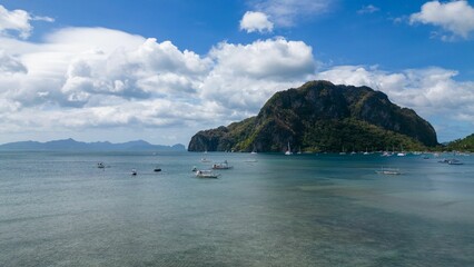 boats floating in the ocean on a blue cloudy day with some rocks in the water
