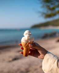 Ice Cream cone in a hand holding with tropical beach background, sunny hot summer time, travel tourism holiday vacation concept.