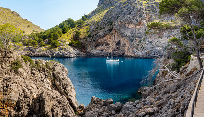 Cala de Sa Calobra bay featuring an idyllic scene of an anchored sailboat in calm blue waters and Turmàs mountain in background, ideal for promoting leisure and travel in Mallorca scenic landscapes.