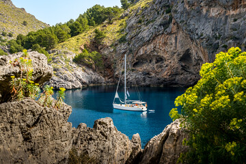 Tranquil beauty of the morning in Cala de Sa Calobra bay, where an anchored sailboat rests in the serene blue waters, surrounded by rocky formations, a serene glimpse into Mallorca coastal allure.