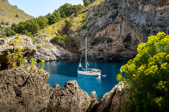 Tranquil beauty of the morning in Cala de Sa Calobra bay, where an anchored sailboat rests in the serene blue waters, surrounded by rocky formations, a serene glimpse into Mallorca coastal allure.