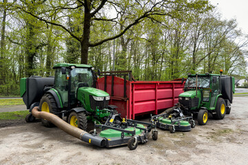 Large green lawn mowers standing near a metal red container. Gray cloudy sky.