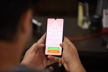 Closeup of male hand holding modern mobile phone with red screen and warning icon with the text 