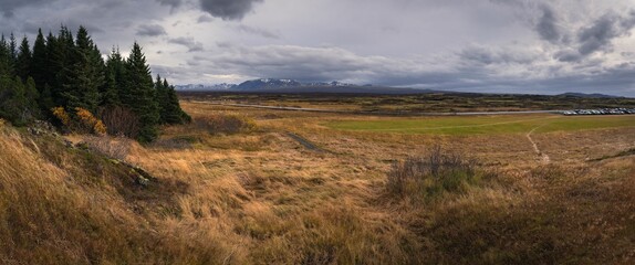 a green field with brown grass on top of it under cloudy skies