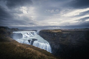 a waterfall that is in the middle of some grass under a cloudy sky