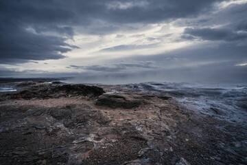 a very dark sky and some rocks by the ocean at dusk