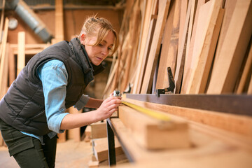 Female Carpenter Working In Woodwork Workshop Measuring Wood For Project