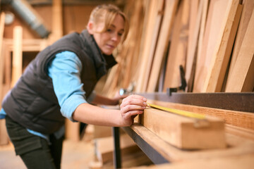 Female Carpenter Working In Woodwork Workshop Measuring Wood For Project
