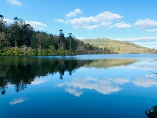 a beautiful lake surrounded by woods on a sunny day with blue sky and clouds