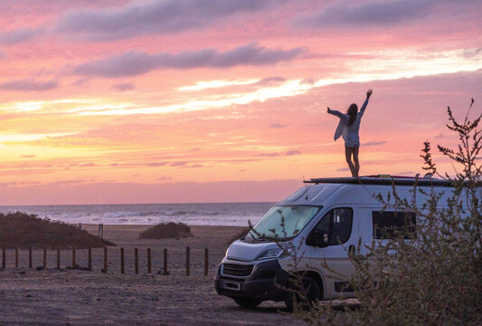 Happy person on camper van roof, embracing sunset by the sea, capturing the essence of travel freedom and adventurous spirit