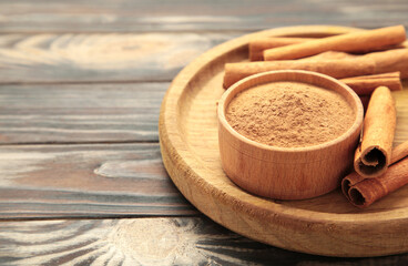 Cinnamon sticks and powder in wooden bowl on brown background. Space for text