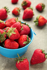 Red fresh strawberry in blue bowl on grey concrete background. Vertical photo