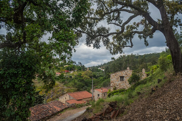 Slope with large oak tree framing the schist village of Água Formosa on a cloudy day, Vila de Rei PORTUGAL