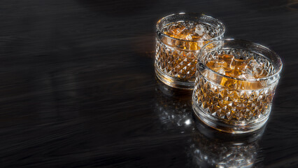3D rendering - Whisky Whiskey Bourbon Scotch Cognac Iced Tea on a pair of shiny diamond-cut ornamented glasses with ice over a dark wooden table