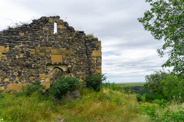 Ruins of an old stone church on the edge of a cliff. Bushes, green and yellow grass.  Samshvilde, Georgia