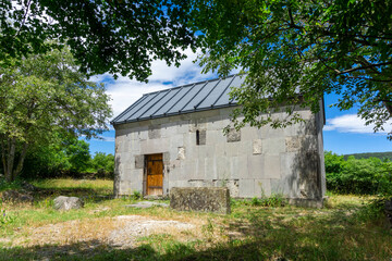 Obraz premium A small church in a meadow in the shade of trees. Wooden door. Large gravestone. Samshvilde, Georgia