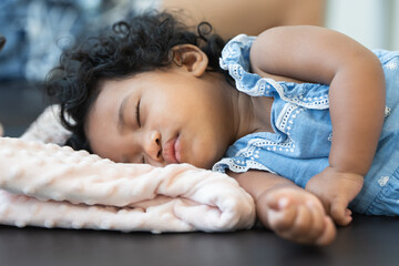 Close up of cute African little newborn 7 months old baby girl with black curly hair, sleeping on...