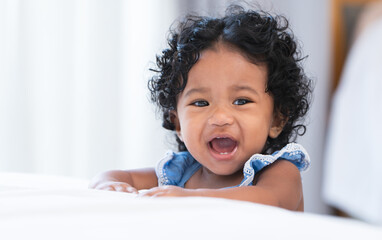 Portrait of adorable African 7 months old newborn baby girl with black curly hair standing near bed...