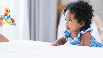 Portrait of adorable African 7 months old newborn baby girl with black curly hair standing near bed...