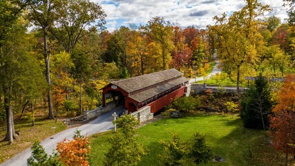 Aerial View of a Burr Truss Covered Bridge Crossing a Stream on an Autumn Day