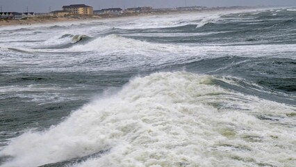 an ocean view with a lot of waves in the foreground and houses in the