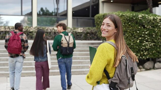Blond student woman going to classes with group of college friends walking towards University building