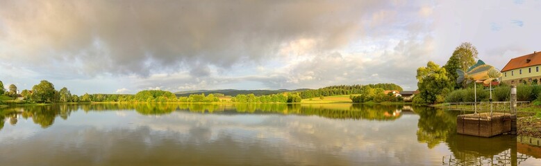 Panoramic of green trees reflecting on a tranquil lake on a sunny day