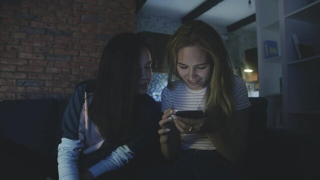 Happy friends sitting on sofa and looking at screen of mobile phone or smartphone. Quarantine using modern technology. Connecting through social networks or messages during epidemic. phubbing concept.